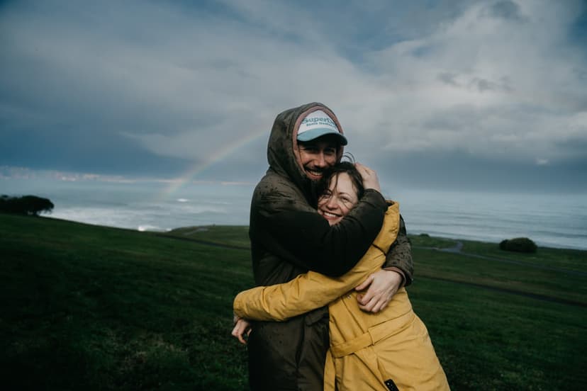 Пара обнимается на фоне океана и радуги в Хихоне, Испания.